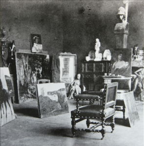 An aged photograph of the painter's studio, filled with paintings, sculptures, and a lone chair.