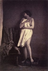 A daguerreotype of a nude poser, clutching a piece of fabric to cover her body.