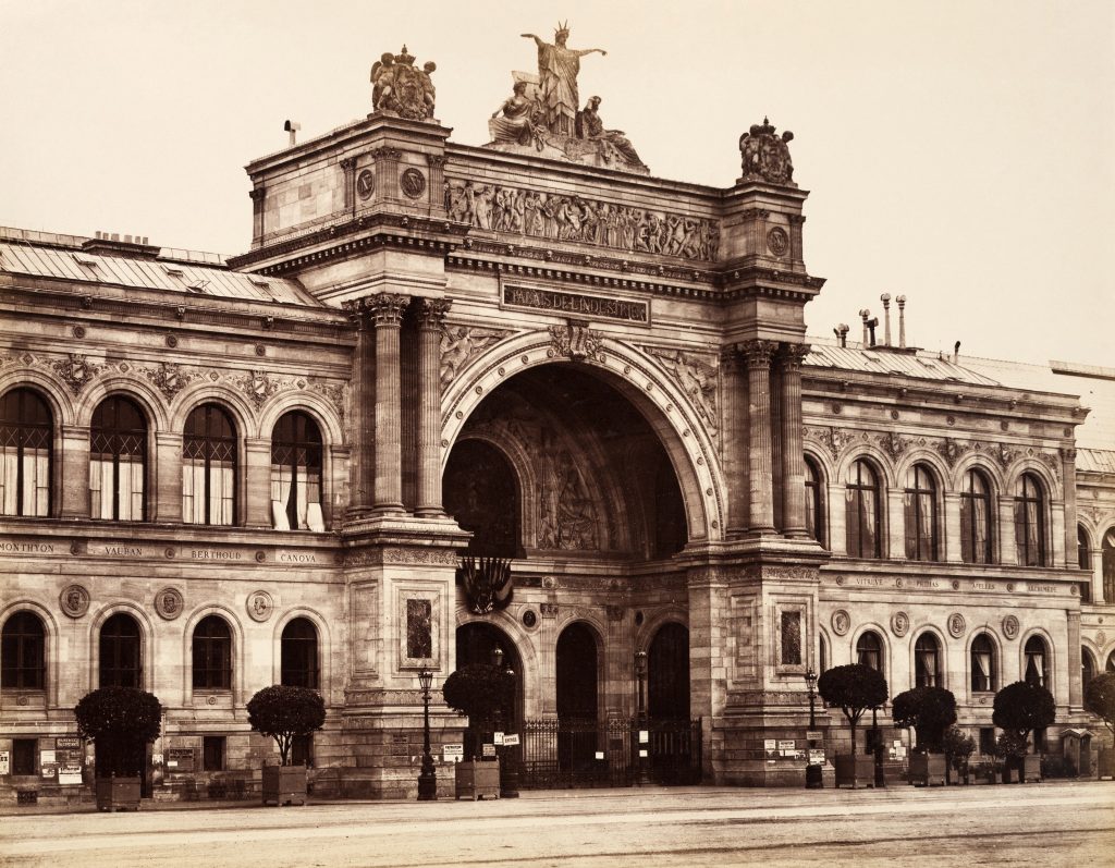 An albumen silver print of a large ornate exhibition hall. On it's arch is written 'PALAIS DE L'INDUSTRIE'.