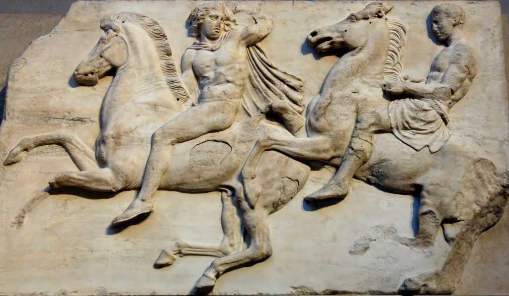 A stone relief of two riders. Both horses have their front legs off the ground.