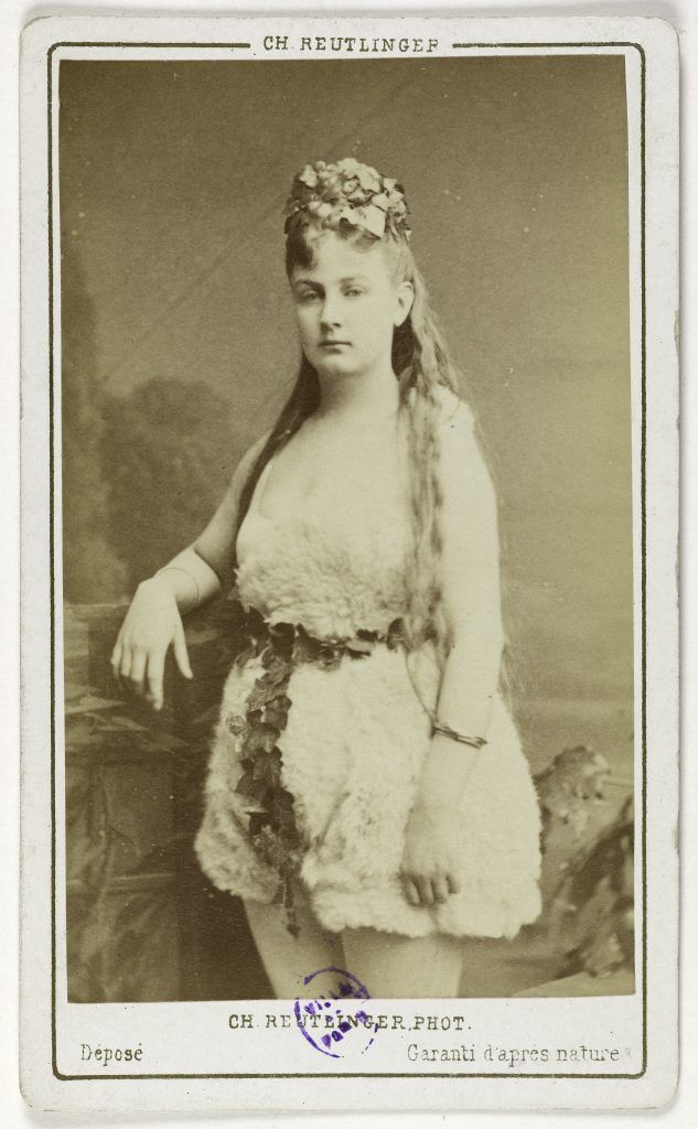 A portrait photograph of a woman in white fur and clad in flowers. Inscribed on the bottom is CH.REUTLINGER.PHOT., and a guarantee of accurate representation.