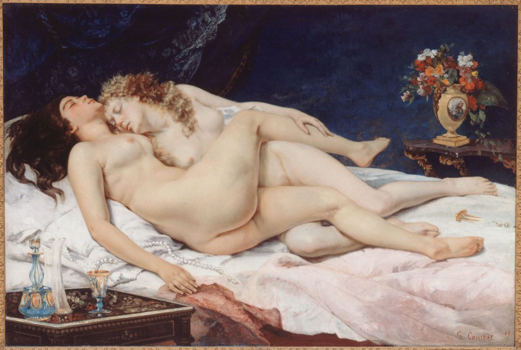 Two nude women, eyes closed in pleasure, embrace each other on a white linen bed. By them is an opulent vase of flowers and candles.