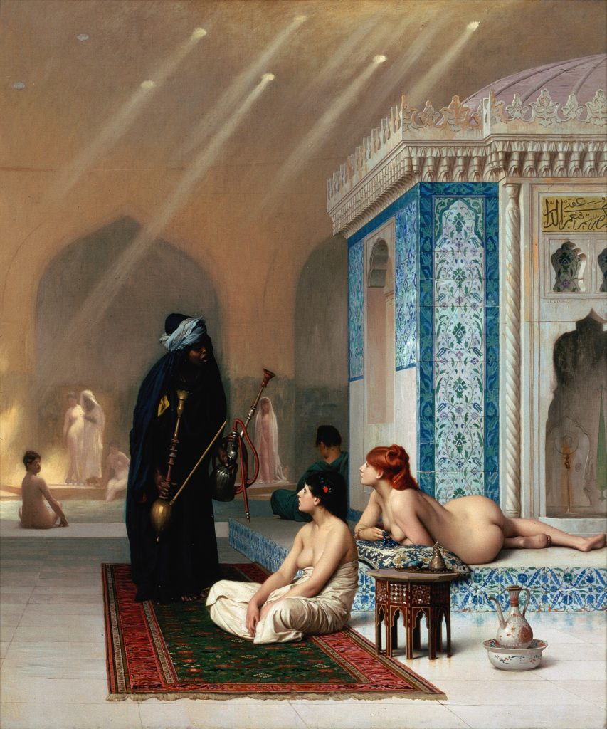 Pale women in states of undress lay around a pool within an oriental lavish palace. A darker skinned servant in cloths brings over a kit for hookah.