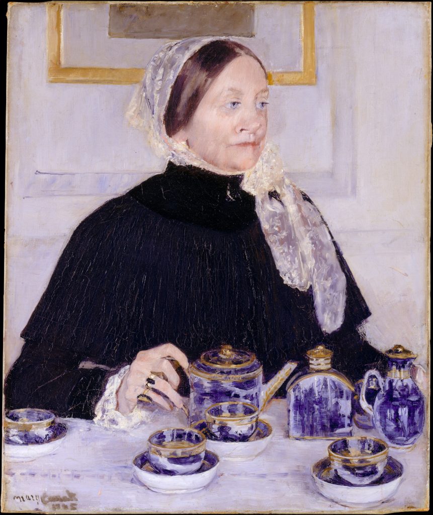 An older woman in a black dress sits by a vibrantly purpled tea set. Her blue eyes peer in judgement to the right.