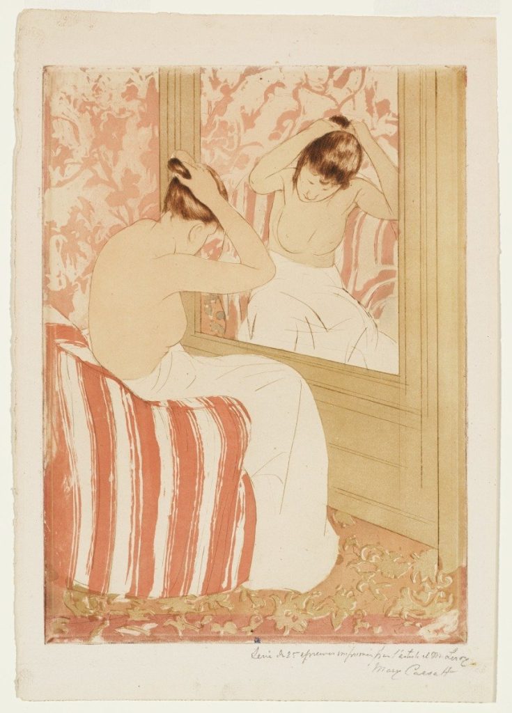 A topless woman ties her hair before a large mirror, a towel drapes her lower half. She is seated in a vibrantly patterned room.