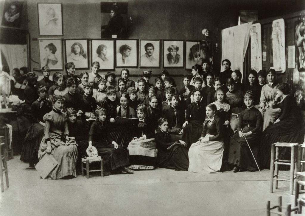 A crowded room of women students in a studio. They wear uniform black dresses.