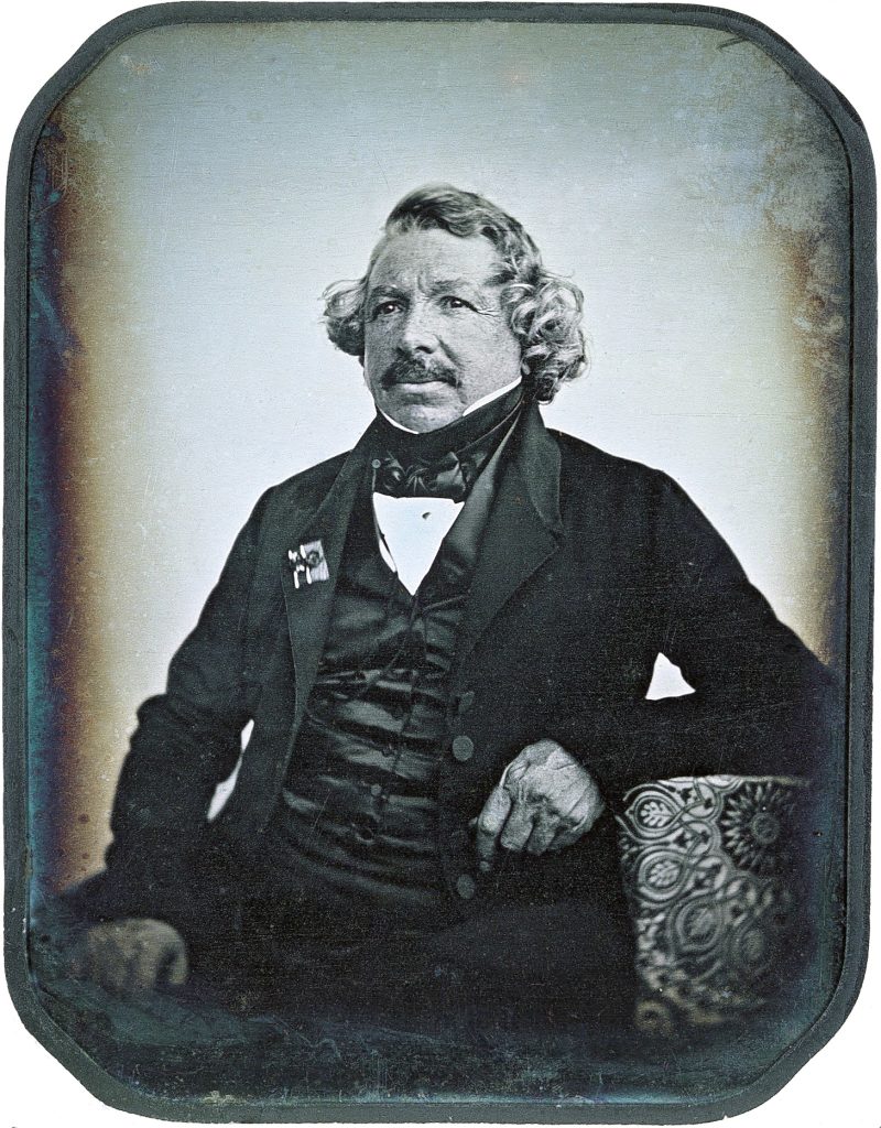 A photographic portrait of a suited man reclined on a sofa. The photo suffered degradation over time.