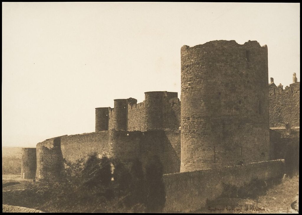 Aged castle walls before a large french country-side. The printed photograph is in a warm beige tone.