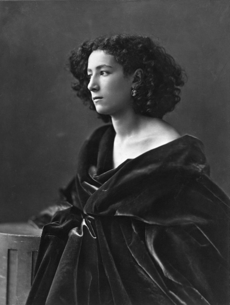 Photographic portrait of a woman in black drapes, curly hair, staring wistfully.