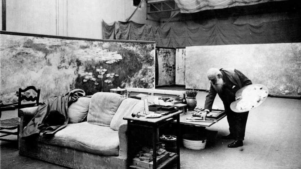 A silver print photograph of Monet at work in his studio, large canvases of water lilies in progress behind him.