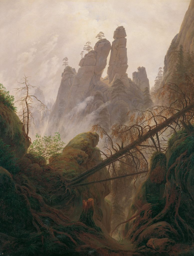A natural scene of a tree, fallen over a ravine cliff-side, before a foggy landscape of upright pillars of mountains.