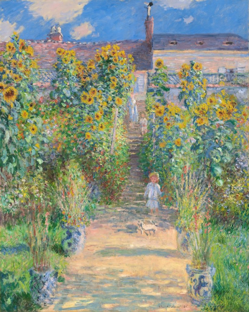 A colourful and bright garden before an estate where a little girl wanders. There is a small dog identifiable.