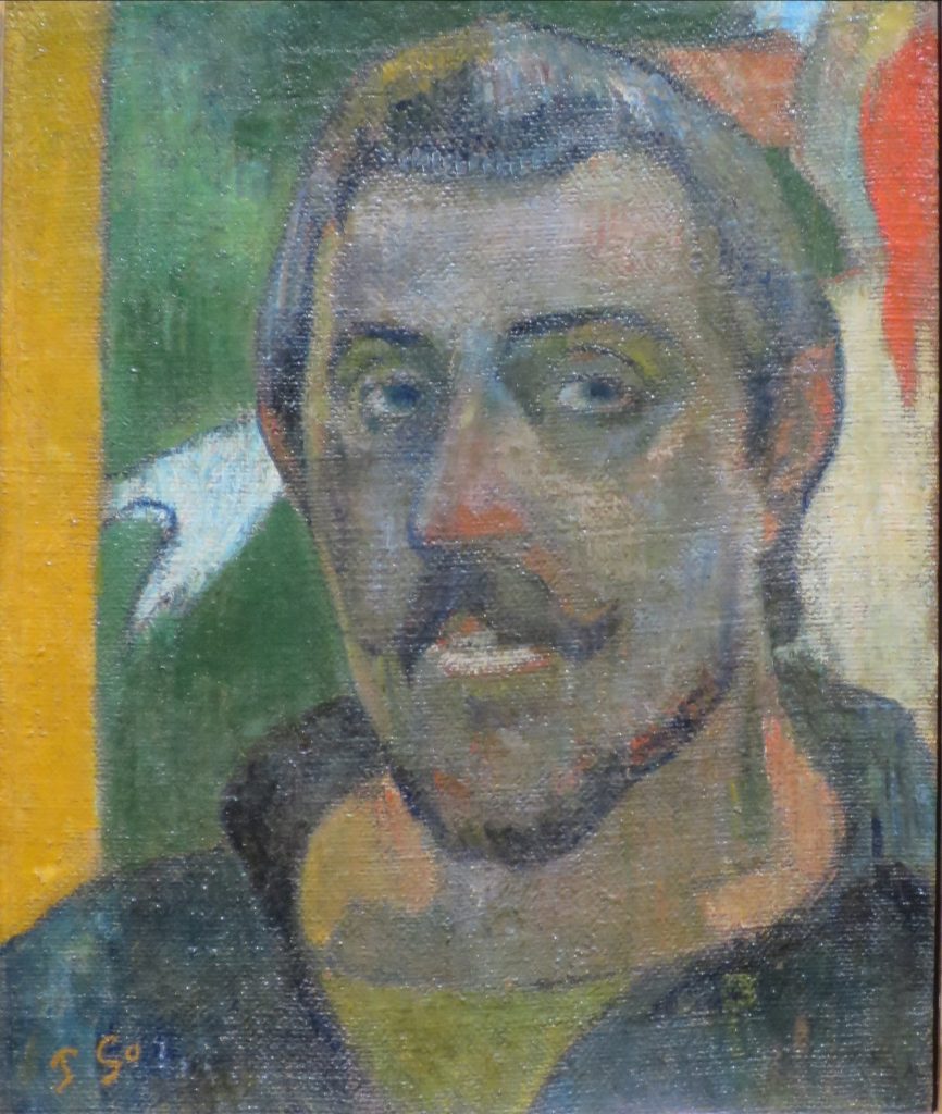 A dark skinned self-portrait before a backdrop alluding to a previous Gauguin painting.