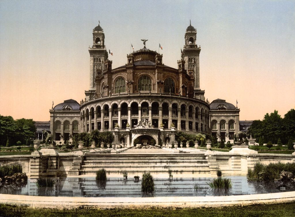An enormous circular palace, beset by pillars, behind a fountain pond.