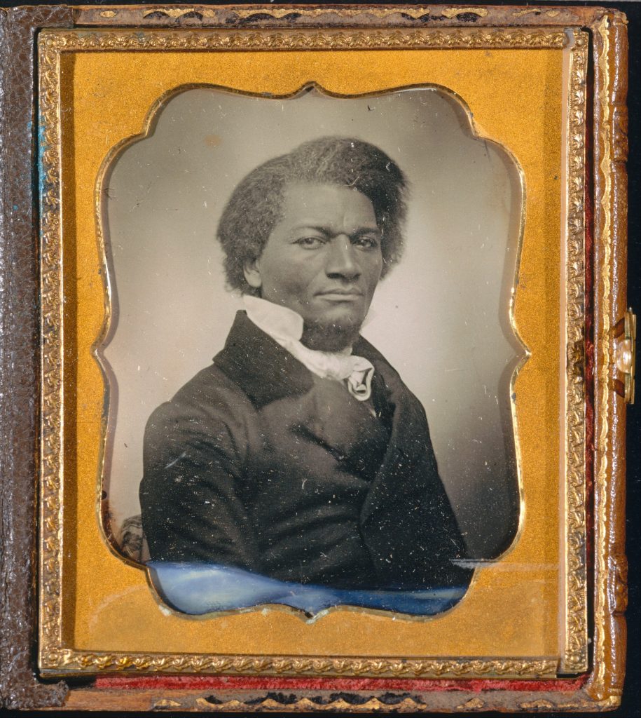 A daguerreotype portrait of Frederick Douglass in a formal black suit, looking to the lens.