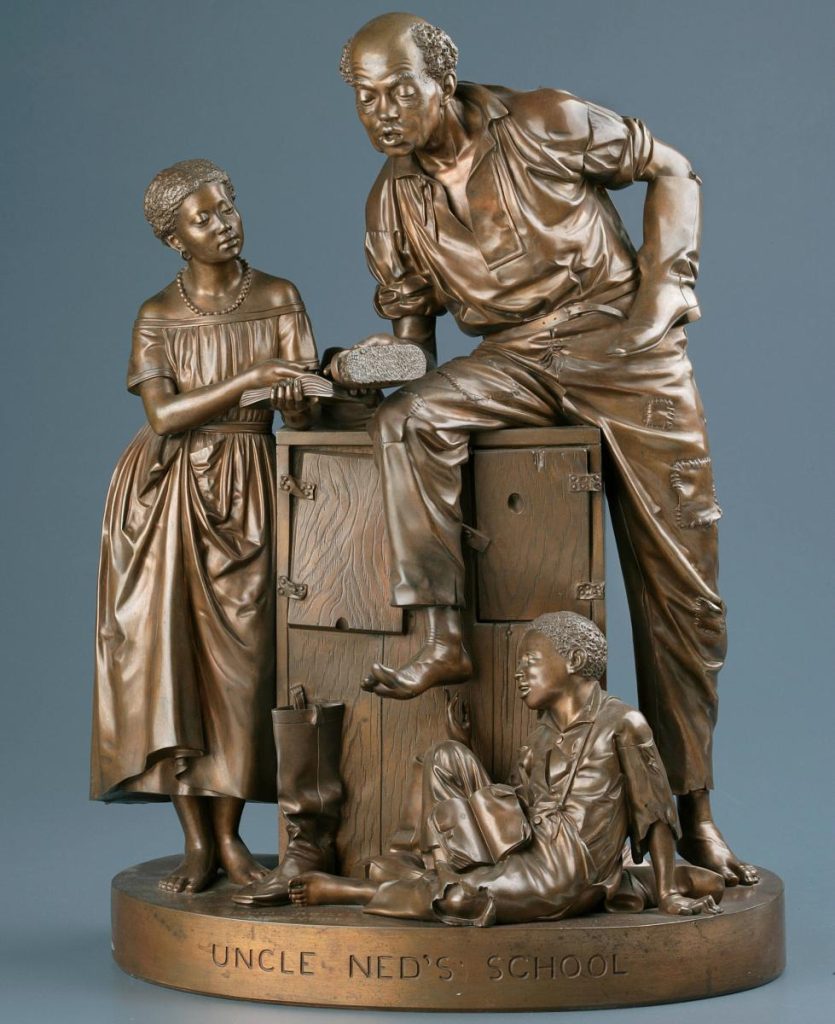 A brass sculpture of a grown black man in worker clothes accompanied by two children, both with books in hand.