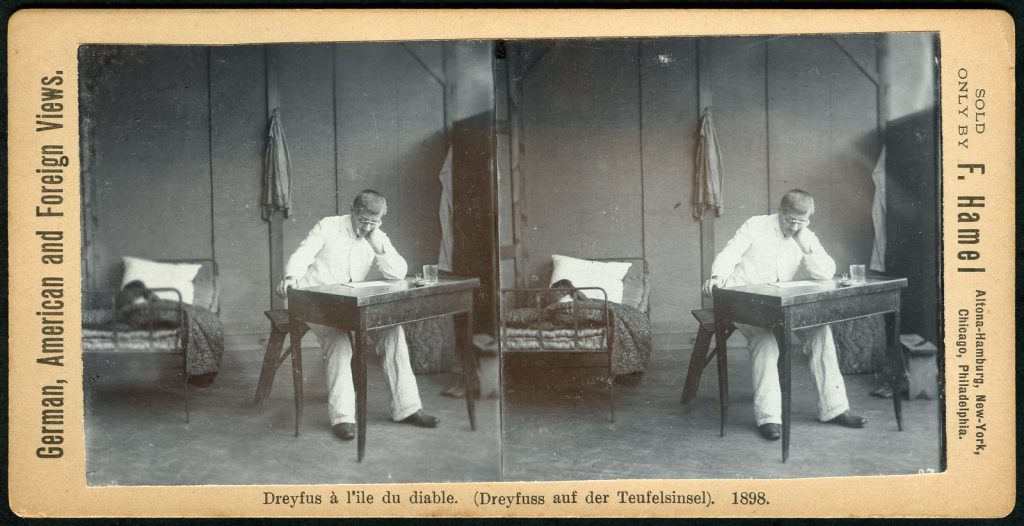 Two photos of Dreyfus in prisoner uniform, sitting at a wooden desk within his cell.