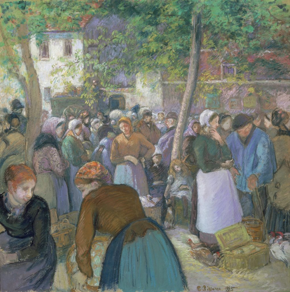 A vibrant and crowded market before a town backdrop, clothing is distinctly coloured.