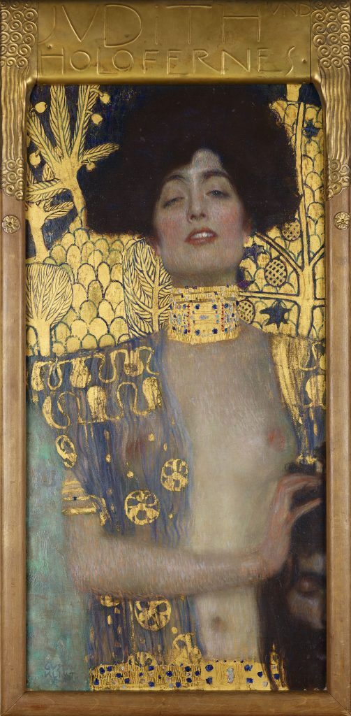 A portrait of a woman poised confidently towards us, nude but gilded in golden natural ornament. Slightly out of the canvas, she clutches a decapitated head.
