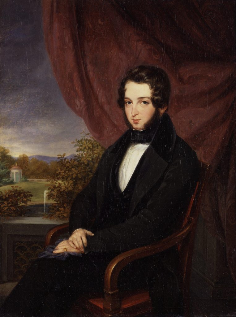 A sat portrait of a formally dressed man sat respectively before a painted landscape. His hands rest politely folded on his lap.