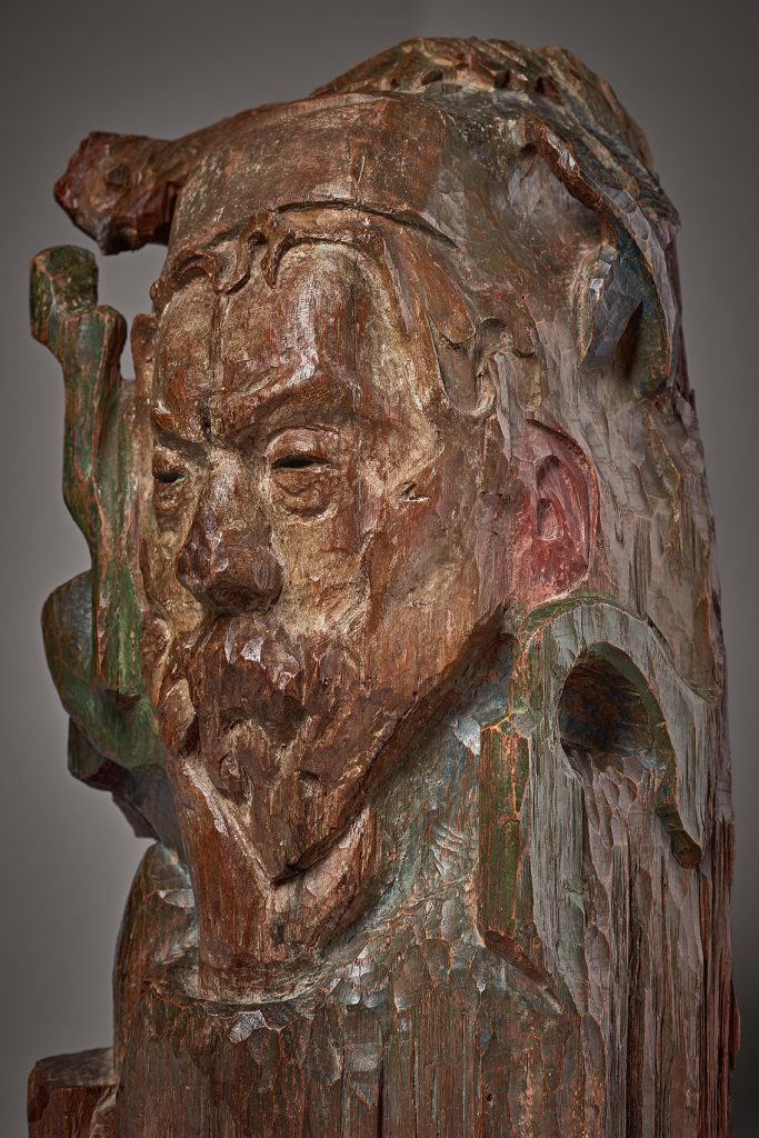 A varnished oak sculpture of de Haan, facial features emerging from the block of wood in precise detail.