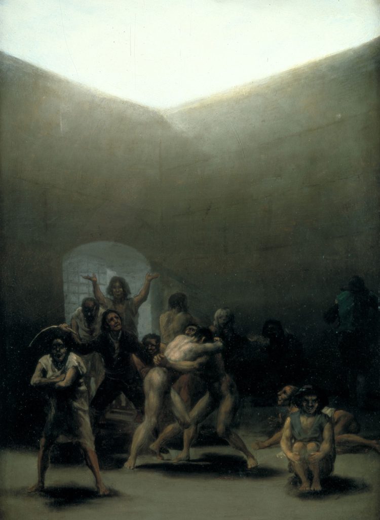 In a sun-lit prison courtyard, two nude men wrestle surrounded by variously posed inmates. Some are obscured by shadow.
