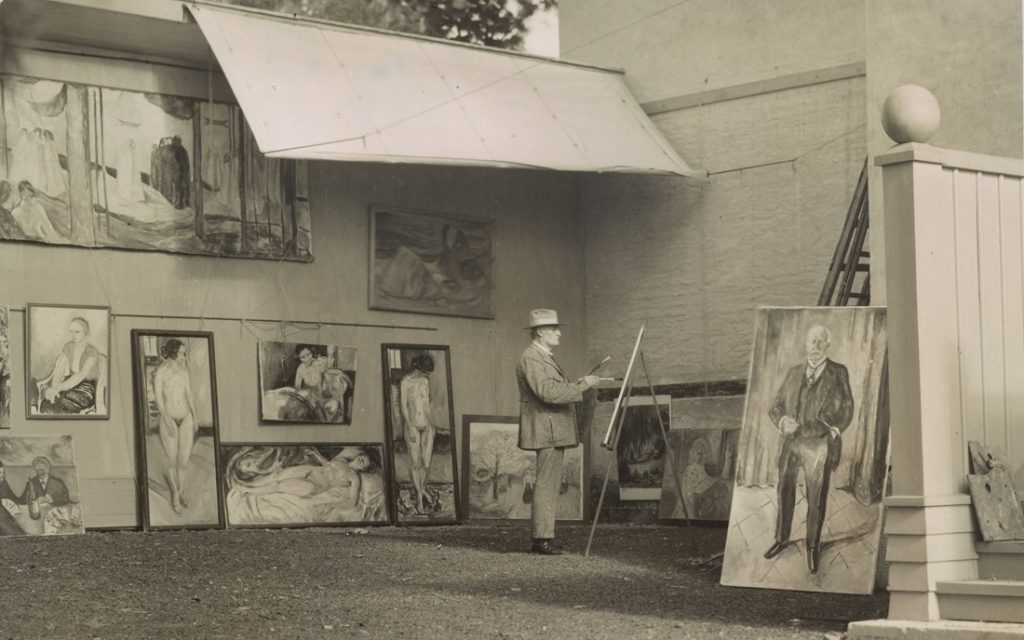 In a grassy courtyard where paintings rest under awning, Munch stands at work.