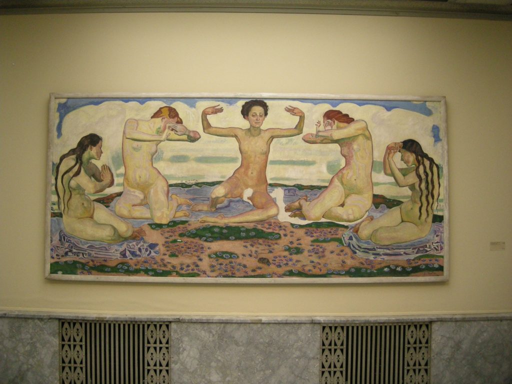 A wide wall-mounted painting of five nude women, arms raised, possibly in prayer. They kneel on pink tapestry on top of flowery landscape.