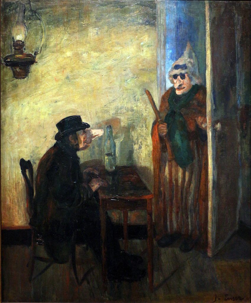 In a lit room, two figures with stretched wax-like face masks engage with one another. One is sat at the table drinking, the other, clutching a stick, enters.