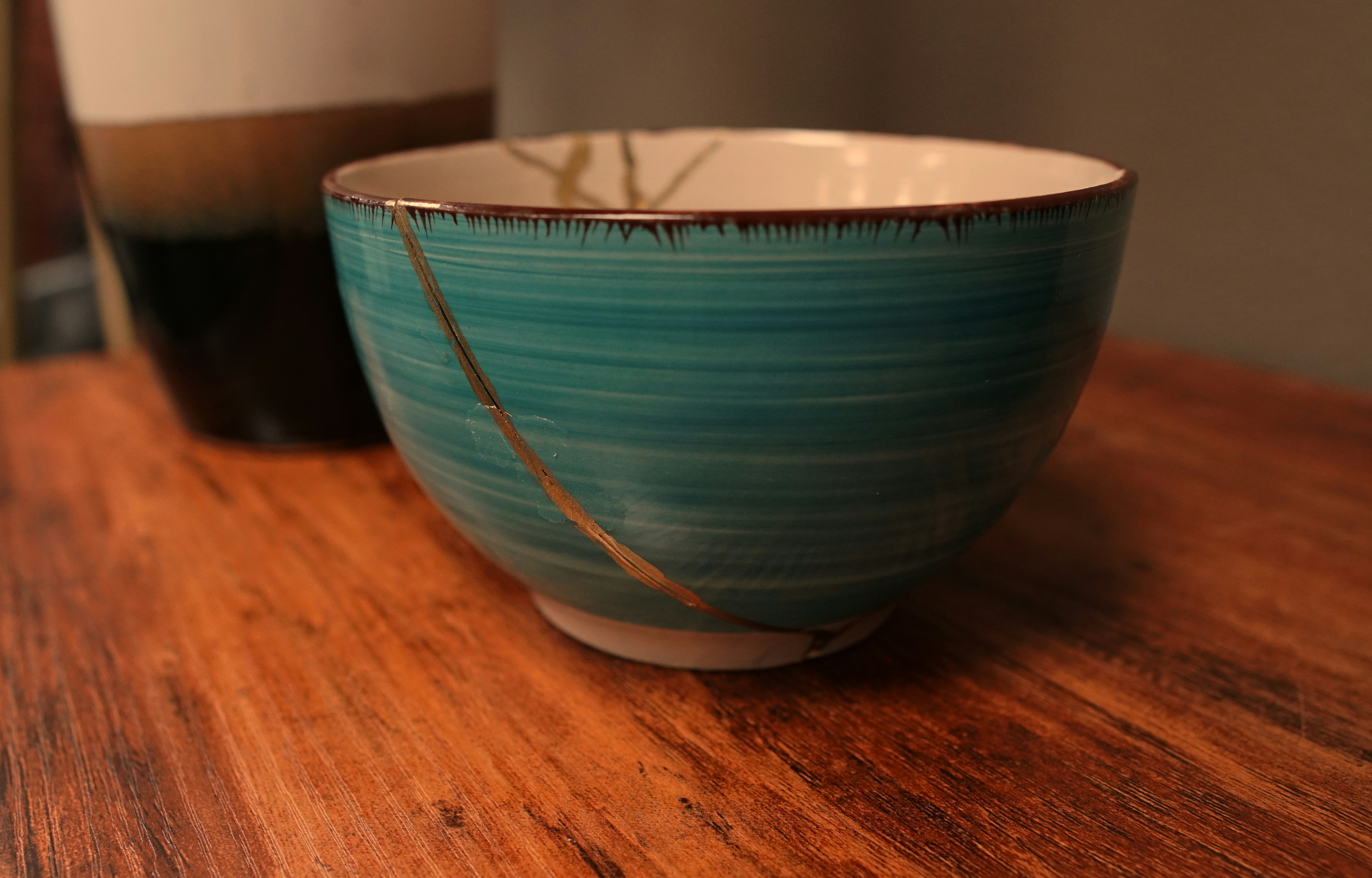 A green ceramic bowl with a crack fixed by gold glue