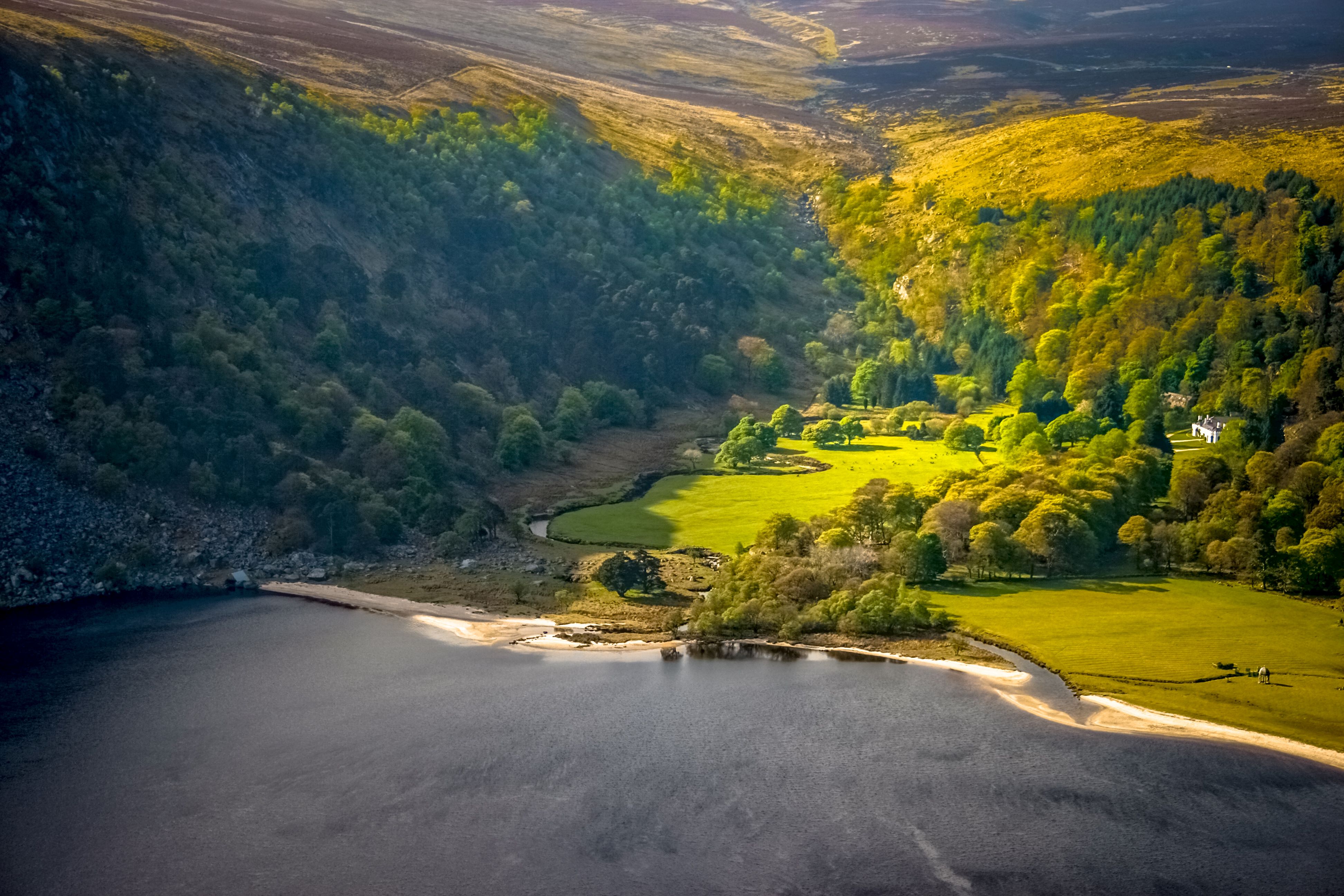 Image of Lough Tay in the Wicklow Mountains. From the middle upwards there are green forested mountains on either side with a descending valley in the middle.