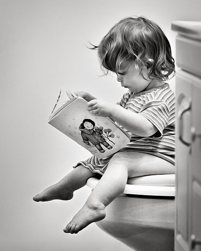 Young infant sitting on a toilet while reading an illustration book