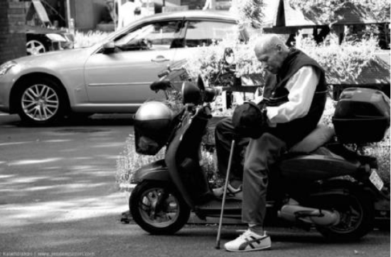 Elder man sitting on a scooter holding his cane.