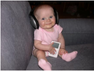 Baby girl wearing headphones while sitting down on a couch and holding an Ipod