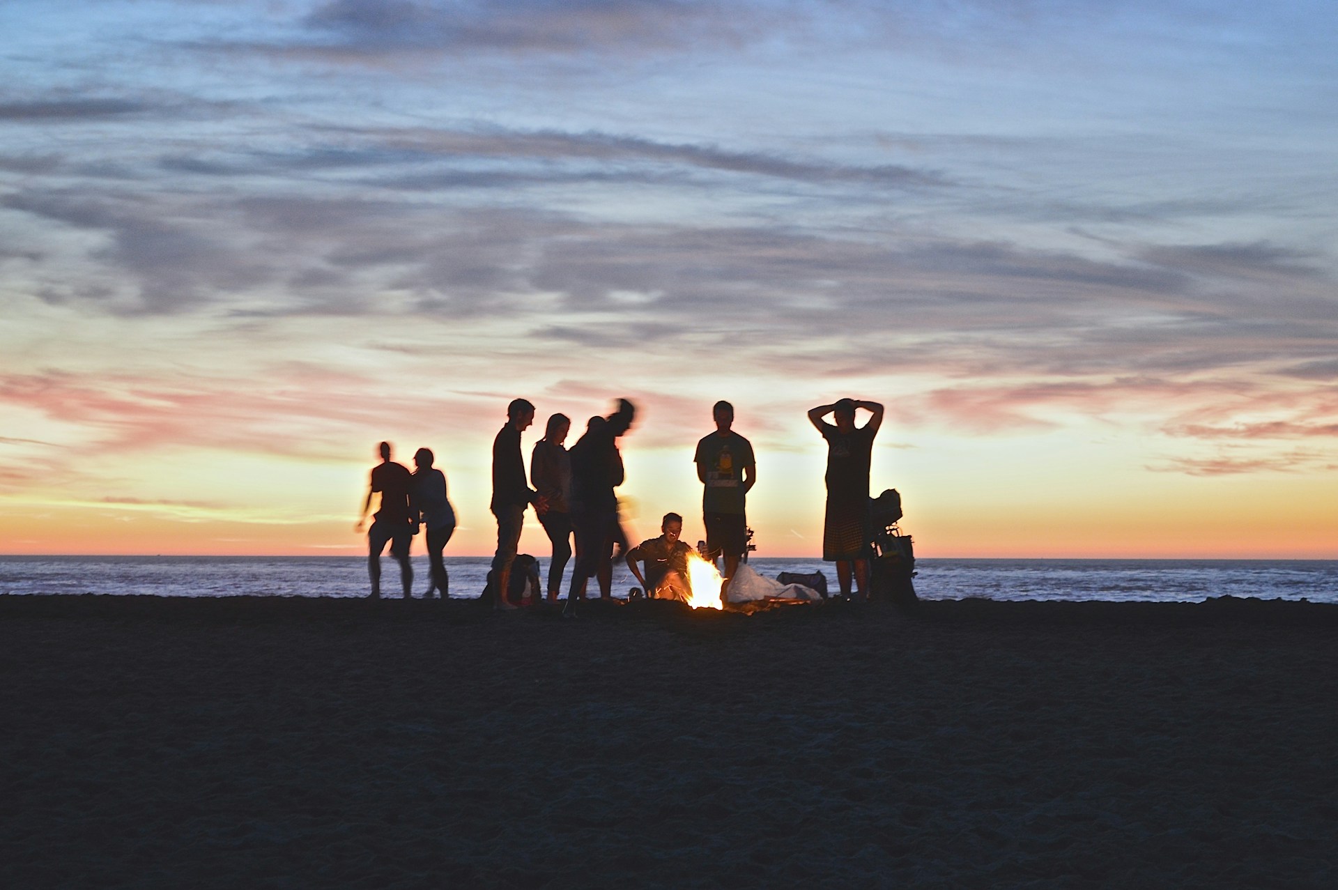 Ten people sitting at a beach bonfire with the sun setting in the distance.
