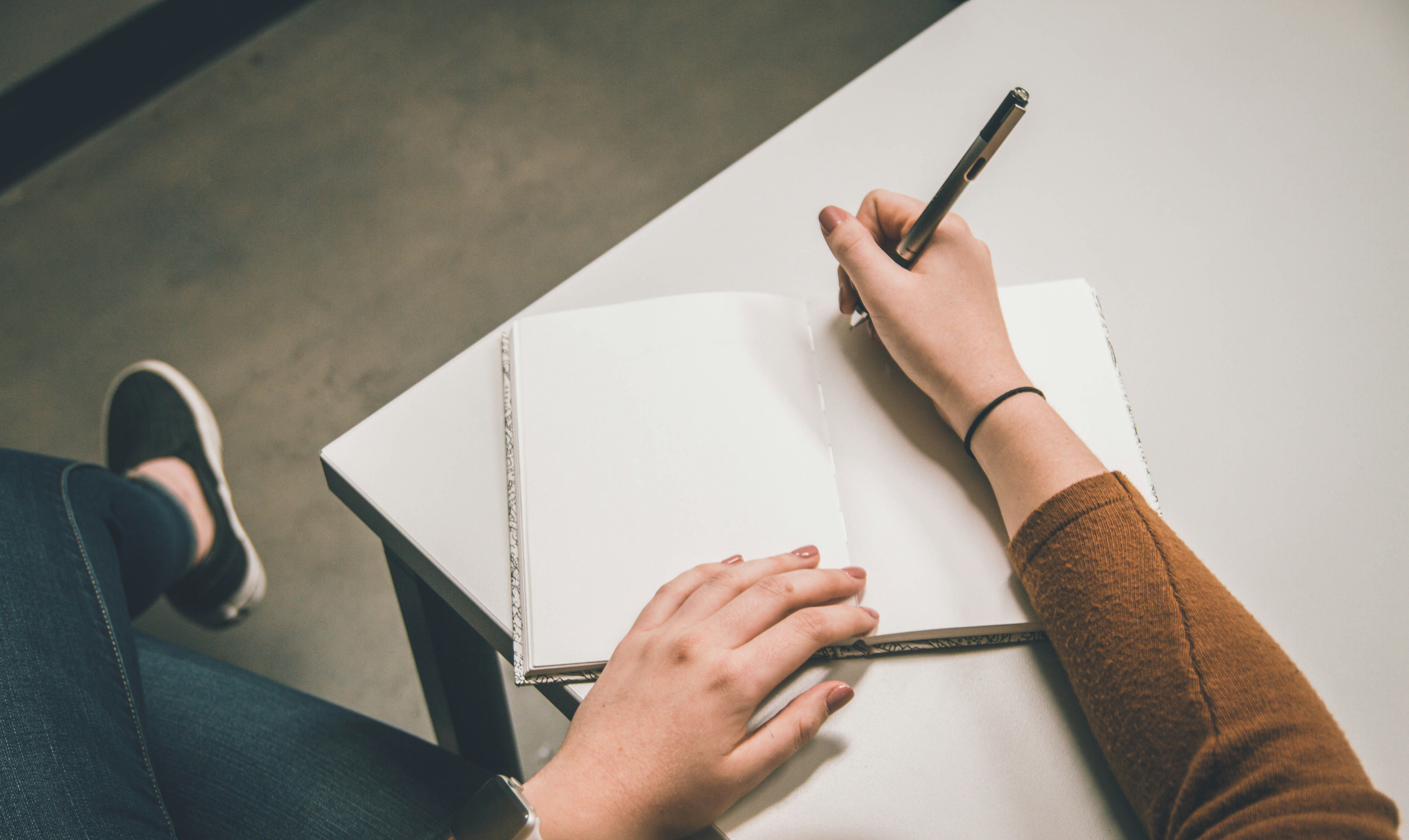 A person with polished nails sitting at a desk, about to write in their blank notebook with a pen.