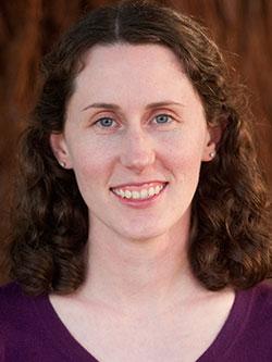 A woman with curly brown, shoulder-length hair smiles at the camera.