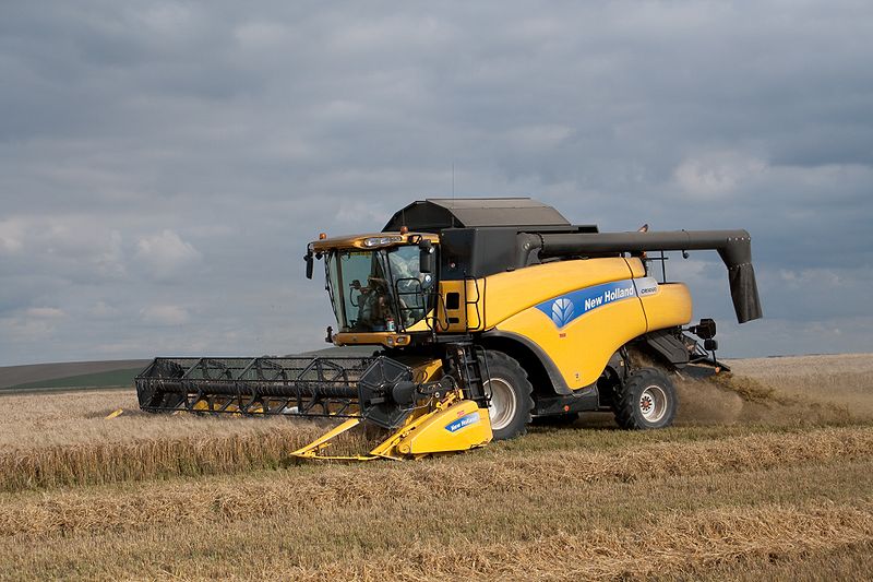 A yellow farm vehicle driving into crops in a field.