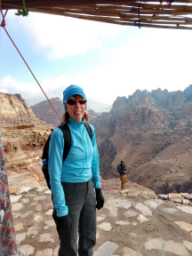 Person wearing outdoor gear including hat and sunglasses with mountains in the background.