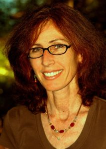 A woman with glasses and brown hair smiles at the camera.