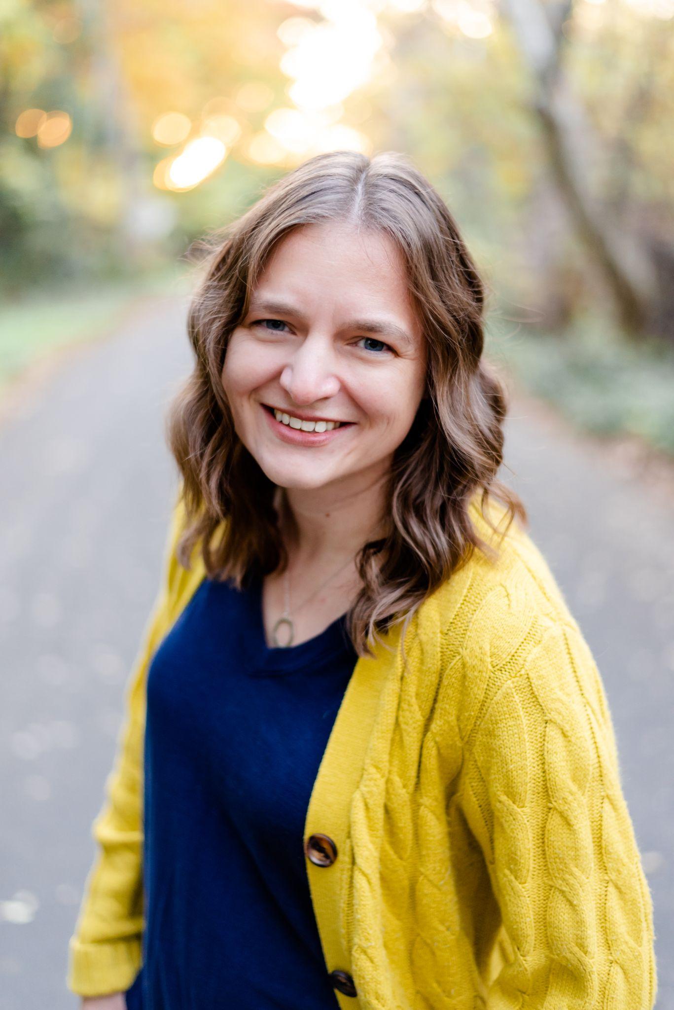 Headshot taken outdoors of smiling person with shoulder length brown hair.