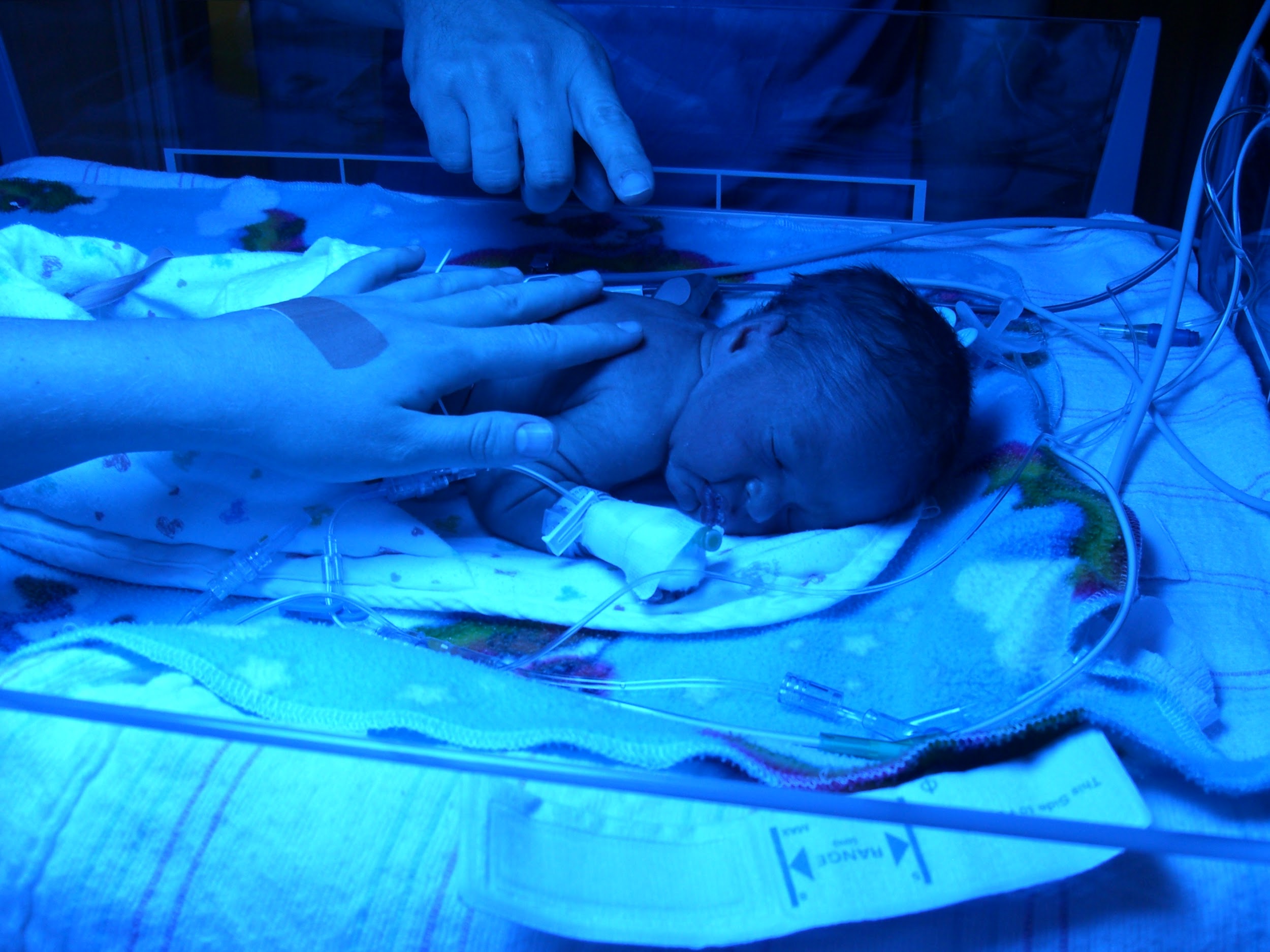 Newborn lays face down on hospital bedding. Photograph is blue indicating UV light.