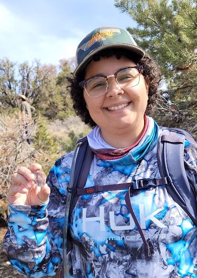 A person with short, curly brown hair and glasses smiles at the camera.