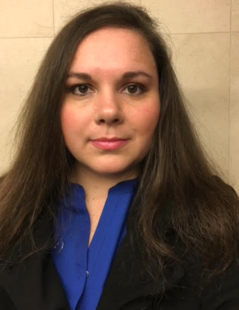 Headshot of author with long brown hair and brown eyes, wearing blue and black.