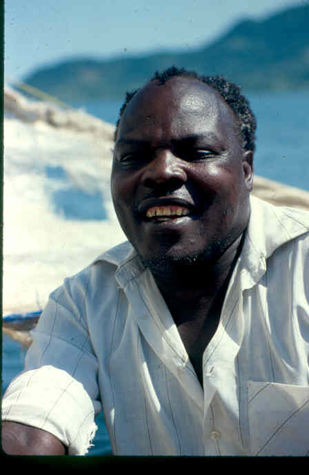 Man smiling at camera with lake and mountain in the background.