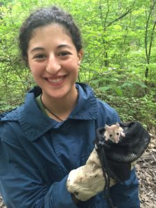 A woman with black hair holds a small mammal wearing gloves.