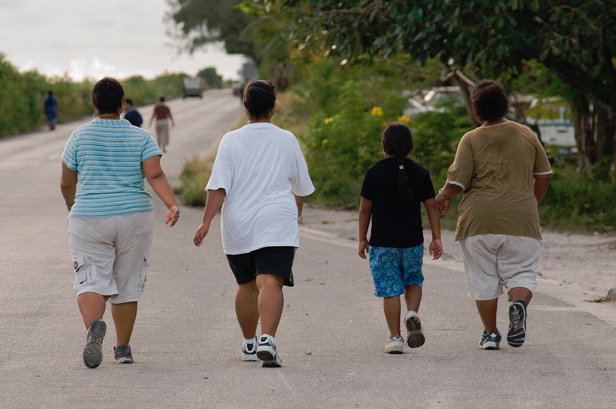 Four individuals of various ages walk alongside trees.