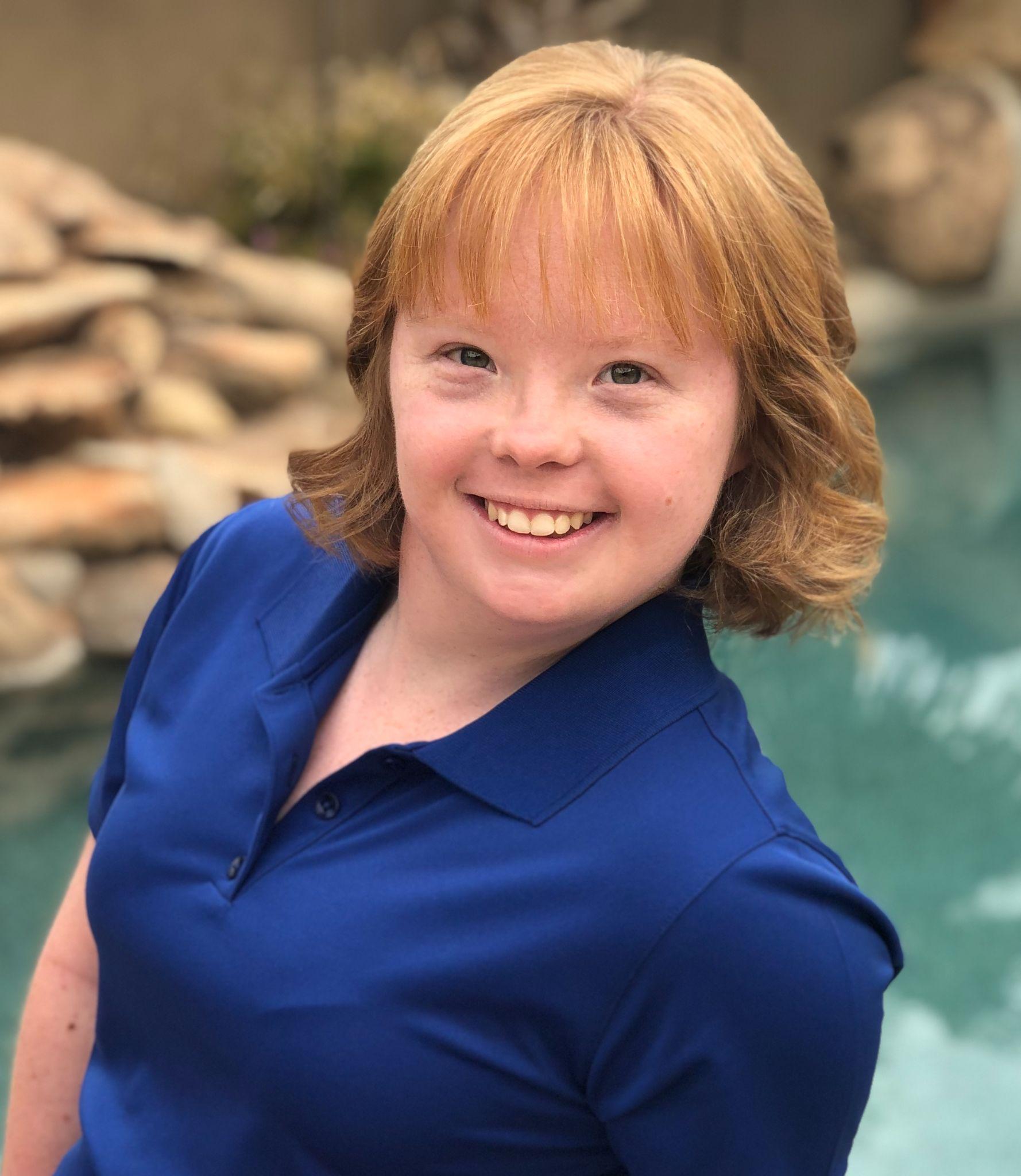 A young woman in a blue polo shirt smiles at the camera.