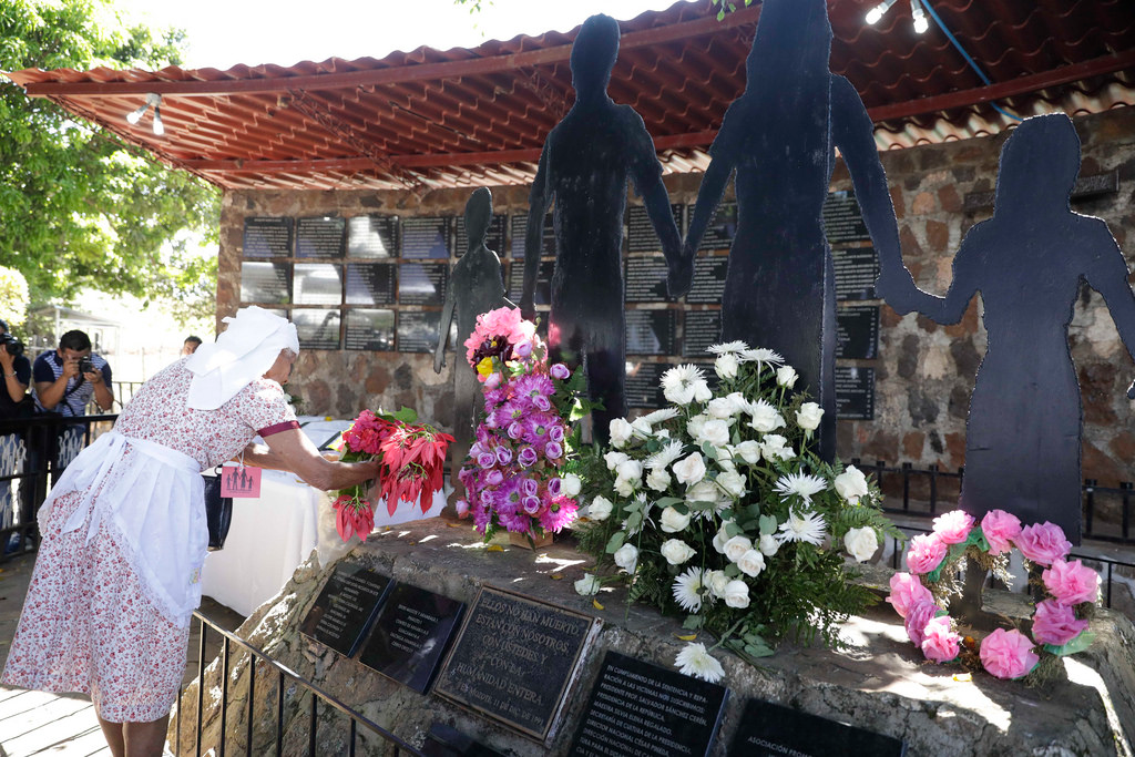 Woman placing flowers near a stone memorial.